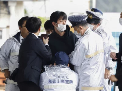 A man, believed to be a suspect who threw a pipe-like object near Japanese Prime Minister Fumio Kishida during his outdoor speech, is held by police officers at Saikazaki fishing port in Wakayama, Wakayama Prefecture, south-western Japan April 15, 2023, in this photo released by Kyodo